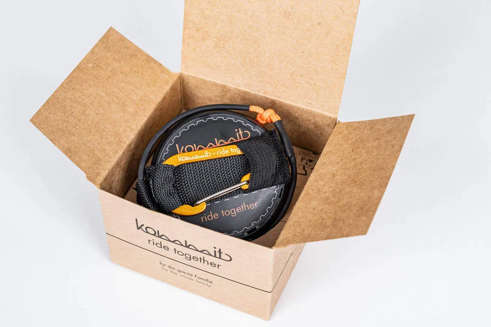 Geöffnete Kartonverpackung zeigt das kommit Zugsystem, ein aufgerolltes Seil mit schwarzer Schlaufe und Karabiner.