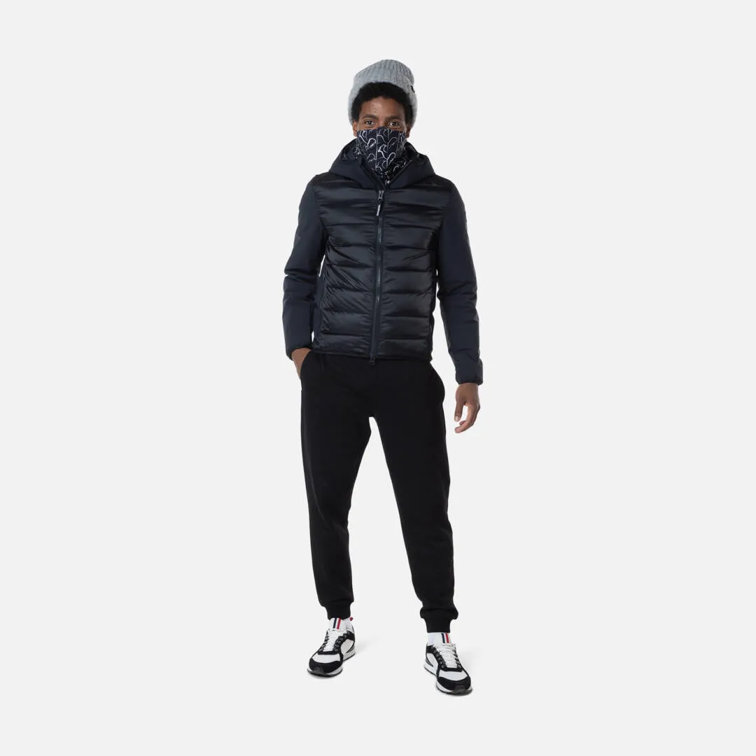 Mann mit Mütze und Muster vor Mund, trägt Rossignol Stretch Quilt Hoodie Jacke in Schwarz, Hose, Turnschuhe.