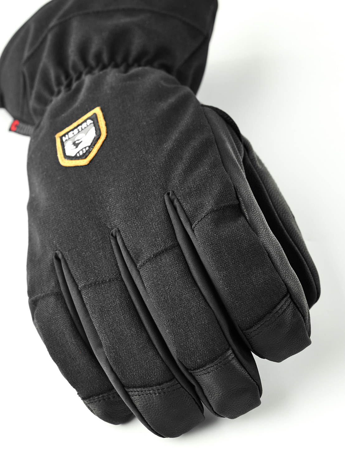Nahaufnahme eines schwarzen Fünf-Finger-Handschuhs mit dem Hestra-Logo auf dem Handrücken.