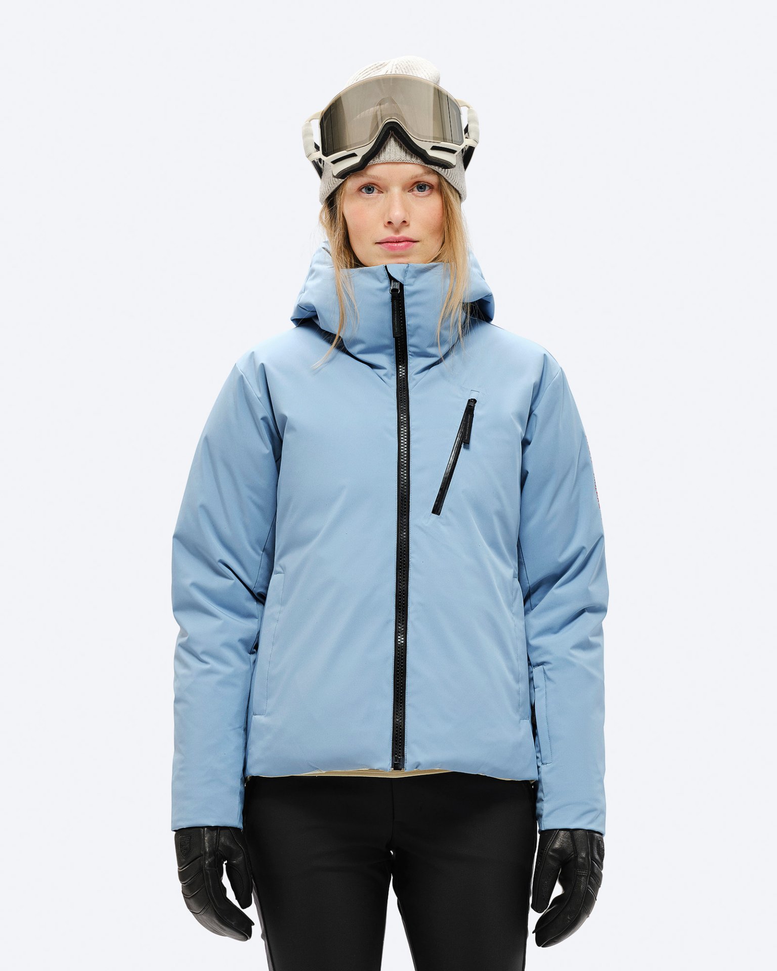 Eine Frau mit Mütze und Skibrille trägt eine hellblaue Daunenjacke mit Kapuze und schwarzem Reißverschluss.
