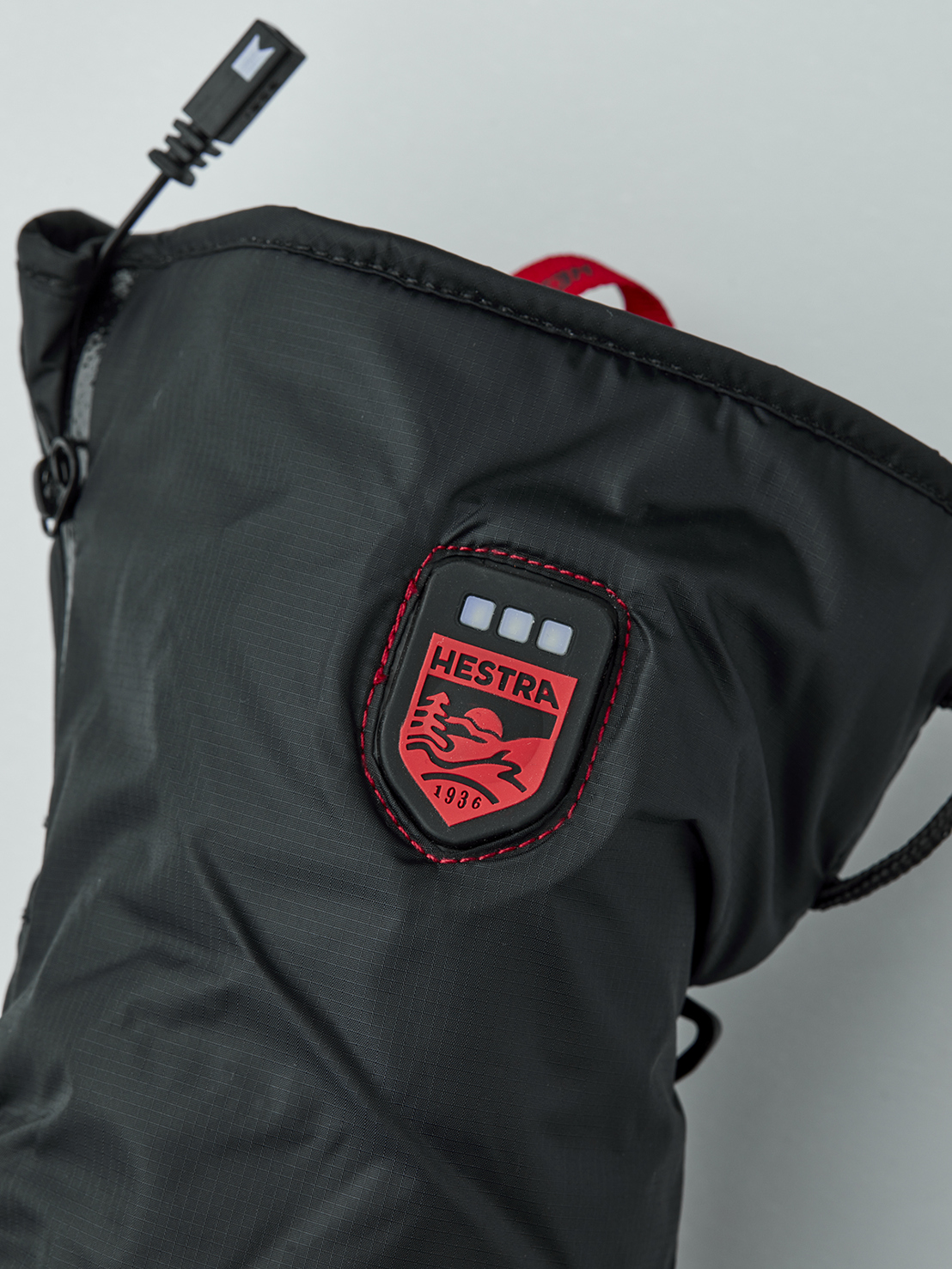 Hestra Heizhandschuh Futter Nahaufnahme eines schwarzen beheizbaren Handschuhfutters der Marke Hestra mit USB-Anschluss und Logo.