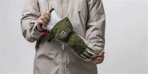 Armeegrün-Handschuh Anprobe Person, die in einen Armeegrün-Handschuh einen Innenhandschuh steckt. Sie trägt eine beige Jacke.